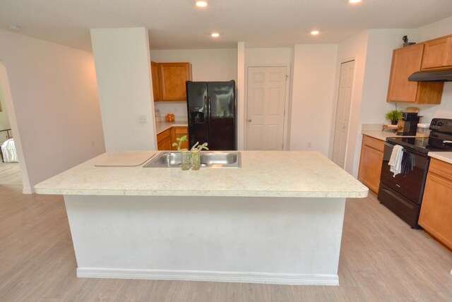 kitchen featuring light wood-type flooring, black appliances, and a kitchen island with sink