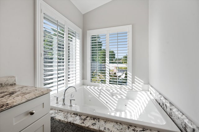 bathroom featuring vanity, vaulted ceiling, a wealth of natural light, and tiled bath