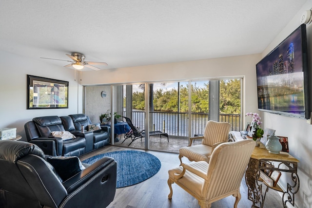 living room featuring ceiling fan, light hardwood / wood-style flooring, and a textured ceiling