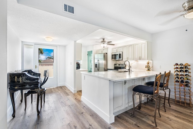 kitchen with kitchen peninsula, ceiling fan, appliances with stainless steel finishes, light hardwood / wood-style floors, and white cabinets