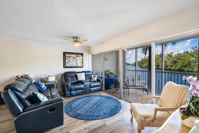 living room featuring light hardwood / wood-style flooring, ceiling fan, and a water view