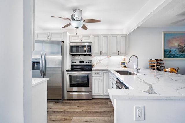 kitchen with sink, appliances with stainless steel finishes, light stone countertops, white cabinetry, and hardwood / wood-style flooring