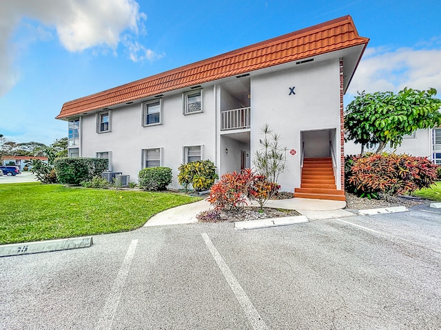 view of front of property featuring a balcony, central air condition unit, and a front lawn