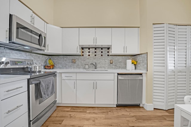 kitchen featuring appliances with stainless steel finishes, light hardwood / wood-style flooring, white cabinets, and backsplash