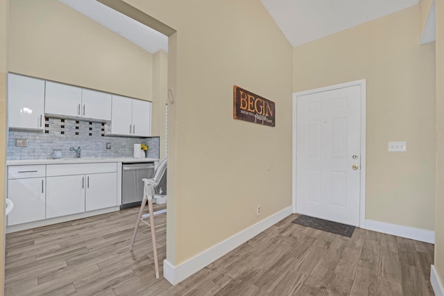 kitchen with white cabinetry, backsplash, stainless steel dishwasher, light hardwood / wood-style floors, and sink