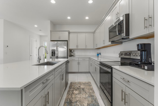 kitchen with sink, an island with sink, light tile floors, stainless steel appliances, and gray cabinets