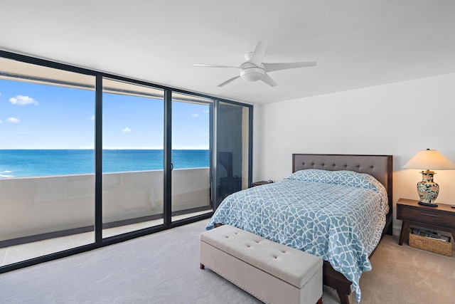 bedroom with a water view, light colored carpet, expansive windows, and ceiling fan