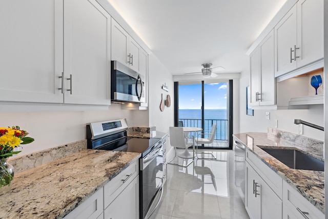 kitchen featuring appliances with stainless steel finishes, white cabinetry, light stone countertops, ceiling fan, and a water view