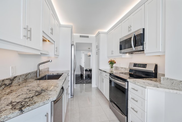 kitchen with stainless steel appliances, white cabinetry, light stone countertops, and sink