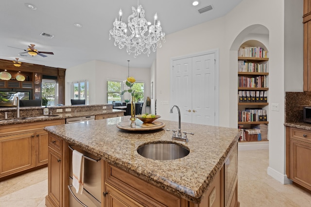 kitchen with a kitchen island with sink, hanging light fixtures, light tile flooring, sink, and light stone counters