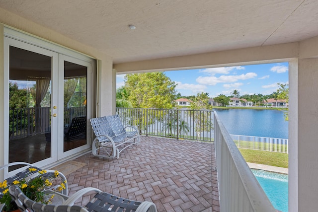 view of patio with french doors, a balcony, a fenced in pool, and a water view