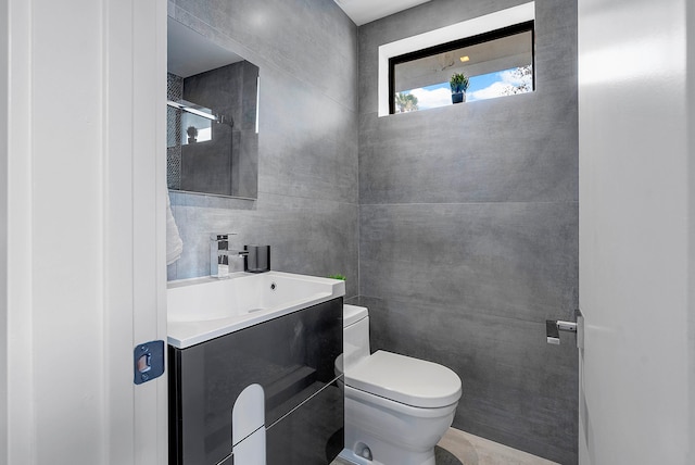 bathroom with vanity, toilet, and tile walls