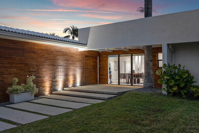 back house at dusk with a lawn and a patio