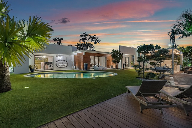 back house at dusk featuring a pool side deck and a yard