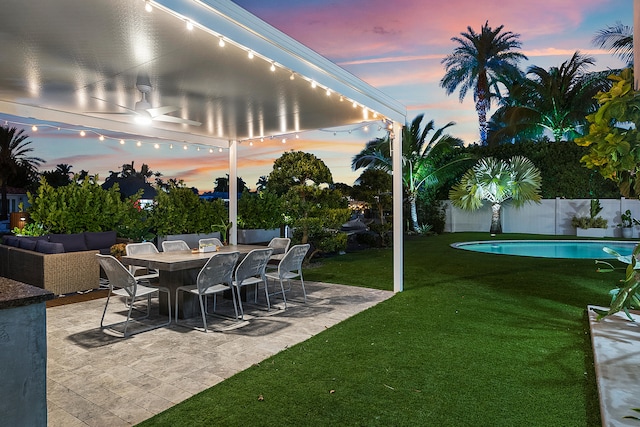 patio terrace at dusk with a lawn and a fenced in pool