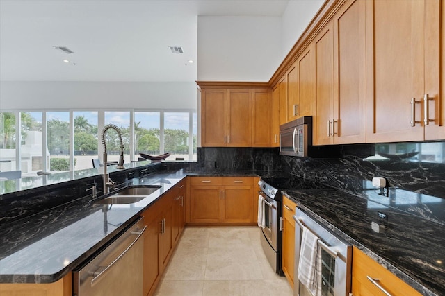 kitchen featuring backsplash, dark stone counters, appliances with stainless steel finishes, and sink