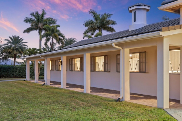 back house at dusk with covered porch and a lawn