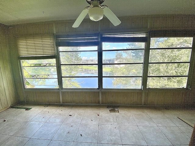 tiled spare room featuring wood walls and ceiling fan