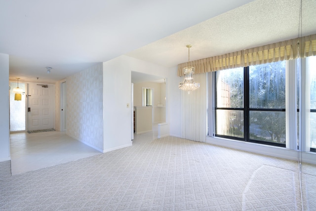 empty room with light carpet, a textured ceiling, and a notable chandelier