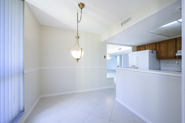 kitchen featuring a textured ceiling, hanging light fixtures, light tile floors, and white refrigerator