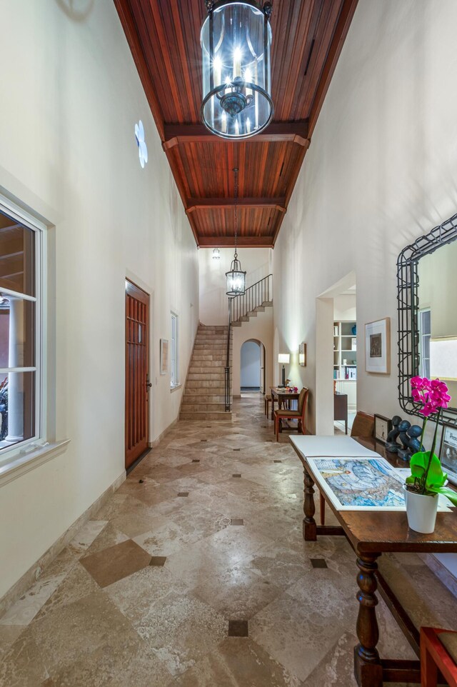 hall with wood ceiling, a notable chandelier, light tile floors, and a high ceiling