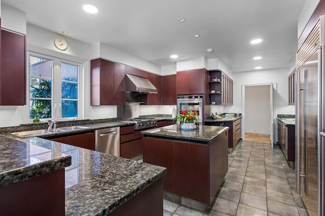 kitchen featuring stainless steel appliances, a center island, wall chimney range hood, light tile flooring, and dark stone countertops