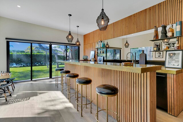 kitchen featuring hanging light fixtures, a kitchen bar, a center island with sink, and light wood-type flooring