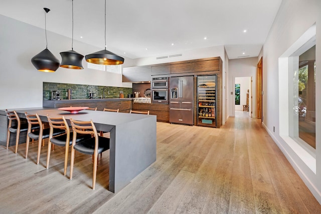 kitchen featuring pendant lighting, a kitchen bar, high quality fridge, light hardwood / wood-style flooring, and sink