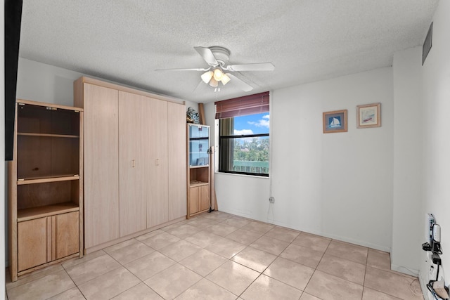 unfurnished bedroom with light tile floors, a textured ceiling, and ceiling fan