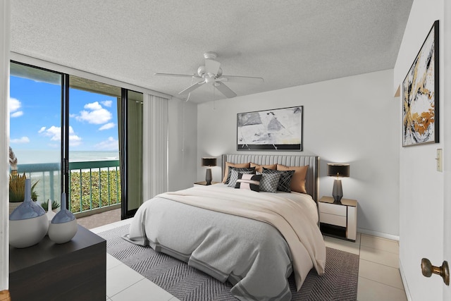 bedroom featuring expansive windows, ceiling fan, a water view, light tile floors, and a textured ceiling