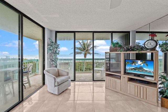 tiled living room featuring ceiling fan, a textured ceiling, a water view, and a wall of windows