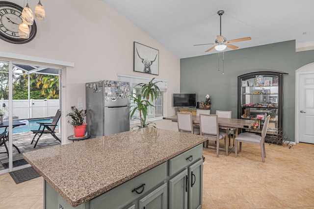 kitchen with vaulted ceiling, ceiling fan, stainless steel fridge, a kitchen island, and light stone counters