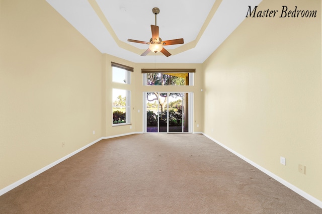 empty room with a raised ceiling, carpet, and ceiling fan