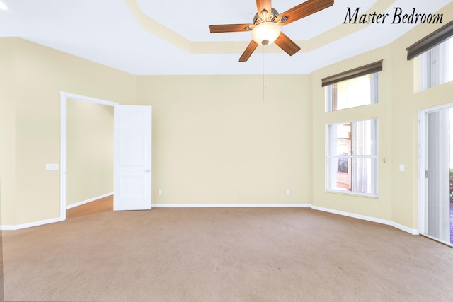 carpeted empty room with a tray ceiling, ceiling fan, and a healthy amount of sunlight