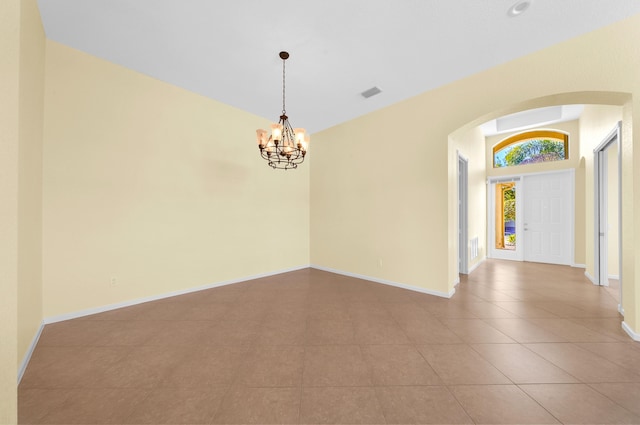 tiled spare room with a chandelier