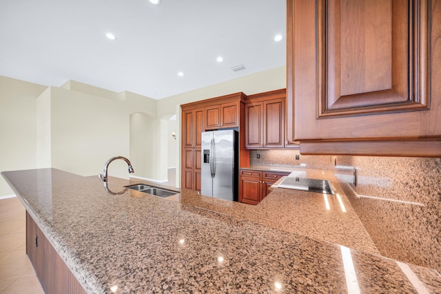 kitchen featuring sink, light tile floors, stone countertops, tasteful backsplash, and stainless steel refrigerator with ice dispenser