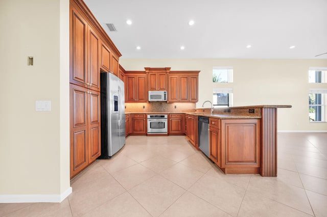 kitchen featuring kitchen peninsula, stainless steel appliances, light tile floors, and light stone countertops