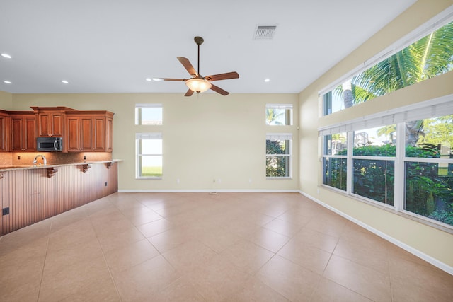 unfurnished living room featuring light tile floors, a towering ceiling, ceiling fan, and sink