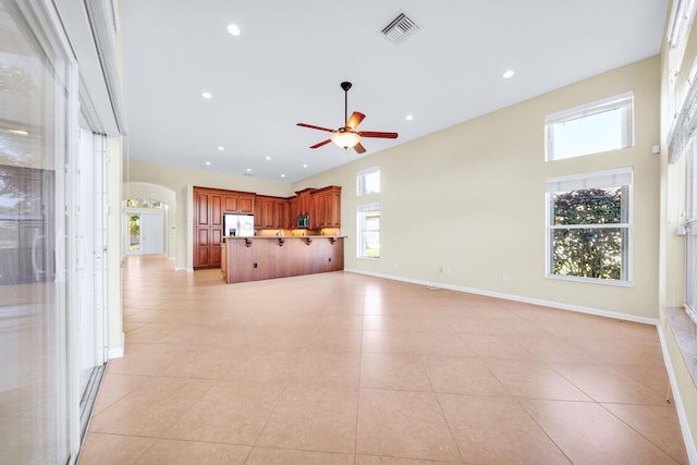 unfurnished living room with ceiling fan, light tile floors, and a high ceiling