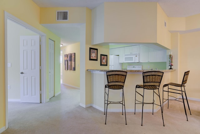 kitchen featuring a kitchen breakfast bar, light carpet, white appliances, a towering ceiling, and white cabinets