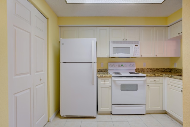 kitchen with light tile floors, light stone countertops, white appliances, and white cabinetry