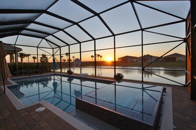 pool at dusk featuring glass enclosure, a patio area, and a hot tub