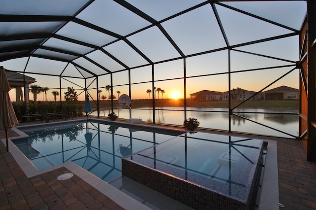 pool at dusk featuring a water view, a lanai, and a patio area