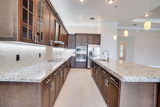 kitchen featuring hanging light fixtures, stainless steel appliances, backsplash, sink, and a kitchen island with sink