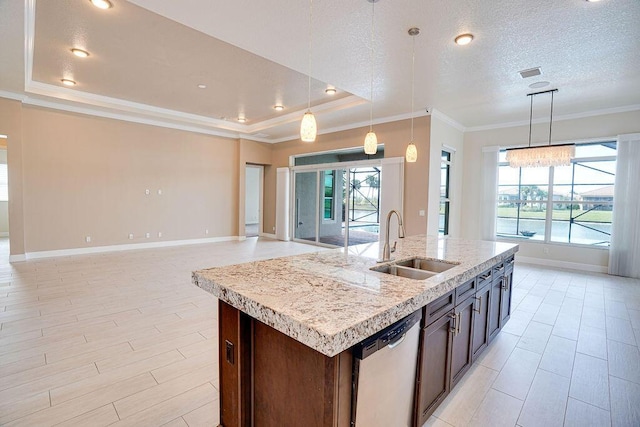 kitchen featuring a center island with sink, sink, a tray ceiling, stainless steel dishwasher, and pendant lighting