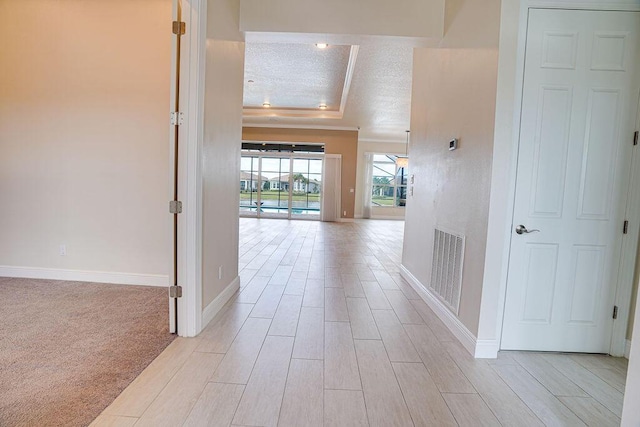 corridor featuring a tray ceiling, crown molding, and a textured ceiling