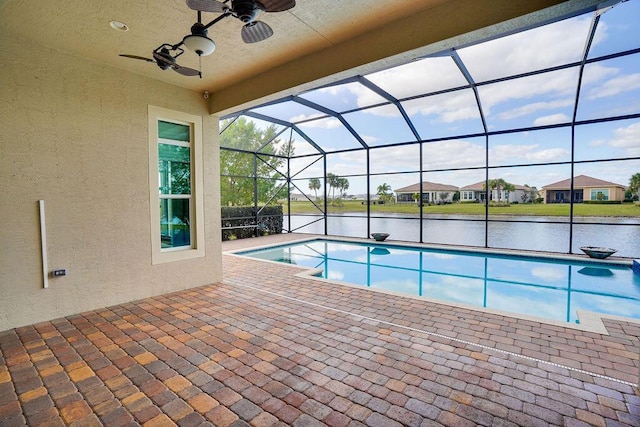 view of swimming pool with a patio, a water view, ceiling fan, and glass enclosure