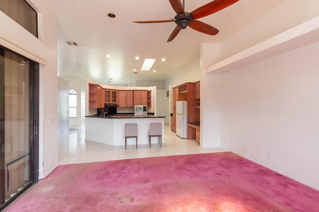 kitchen featuring a kitchen bar, a skylight, stainless steel microwave, white fridge, and light colored carpet