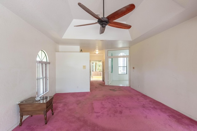 empty room featuring a raised ceiling, vaulted ceiling, carpet flooring, and ceiling fan