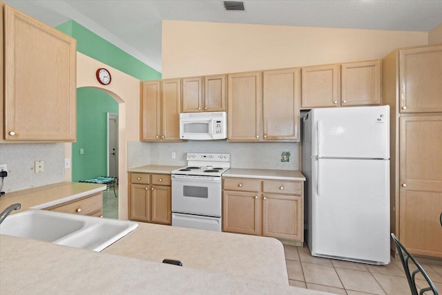 kitchen featuring light tile floors, light brown cabinets, vaulted ceiling, and white appliances